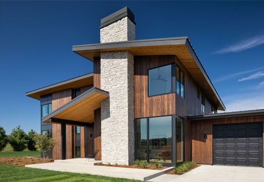 A modernist cedar-clad home with oversized eaves and black floor-to-ceiling windows stands out against the blue skies of a summer’s day.