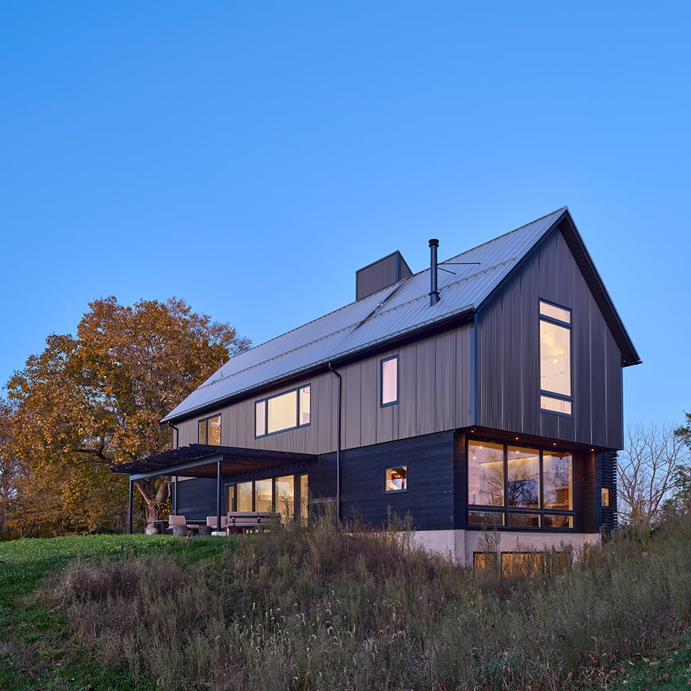 A farmhouse at dusk with an overhang and large picture windows.